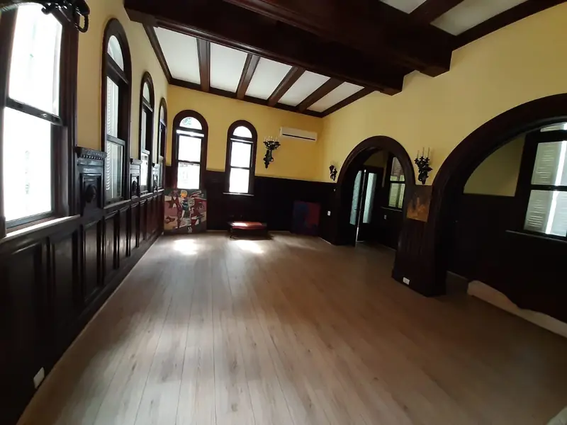 Salão institucional com piso de madeira e janelas altas